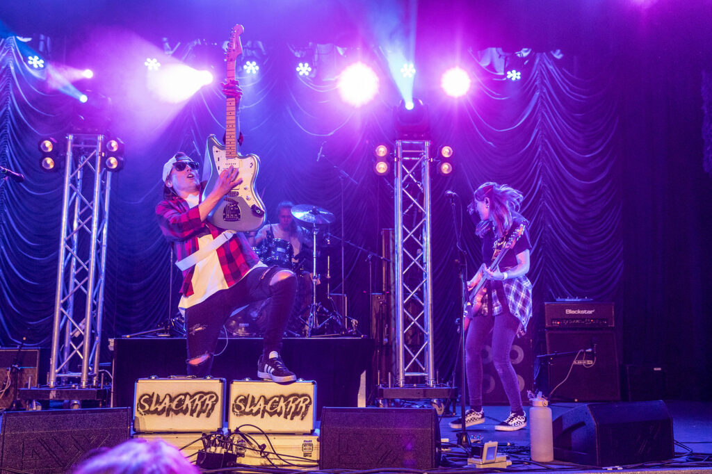 A guitarist holds his guitar aloft and put one foot on the speaker box