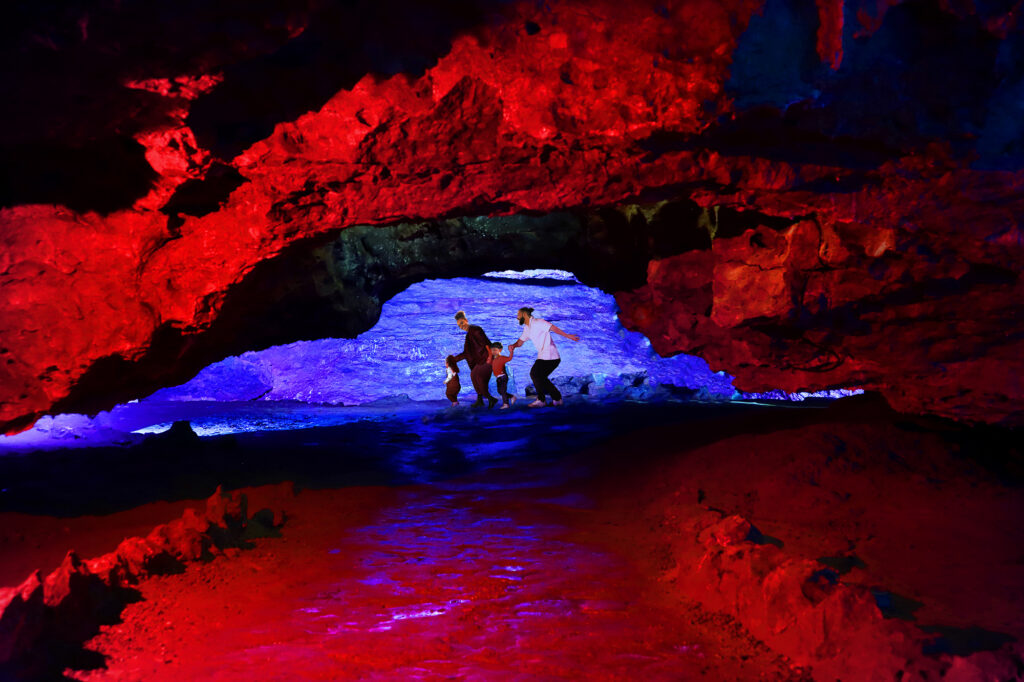 A family of four people underground in Wookey Hole Caves which are illuminated in blue and red