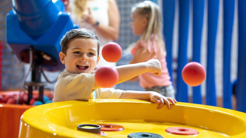 A child enjoying soft play with three red balls in the air