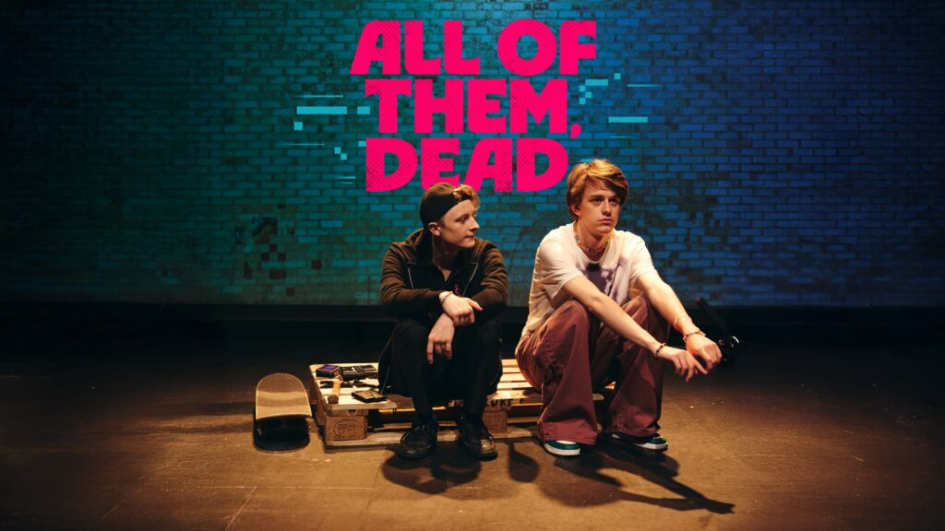 Two people sitting on a pallet in front of a brick wall with the words all of them dead written in red