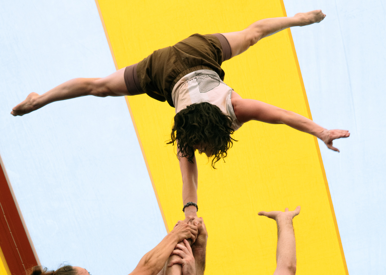 Hands reaching up to support a circus performer who is being held upright and upside-down with legs stretched wide