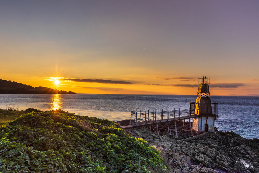 The distinctive Portishead ligthouse which looks like an upside down lantern with the sun setting over the hills in the distance