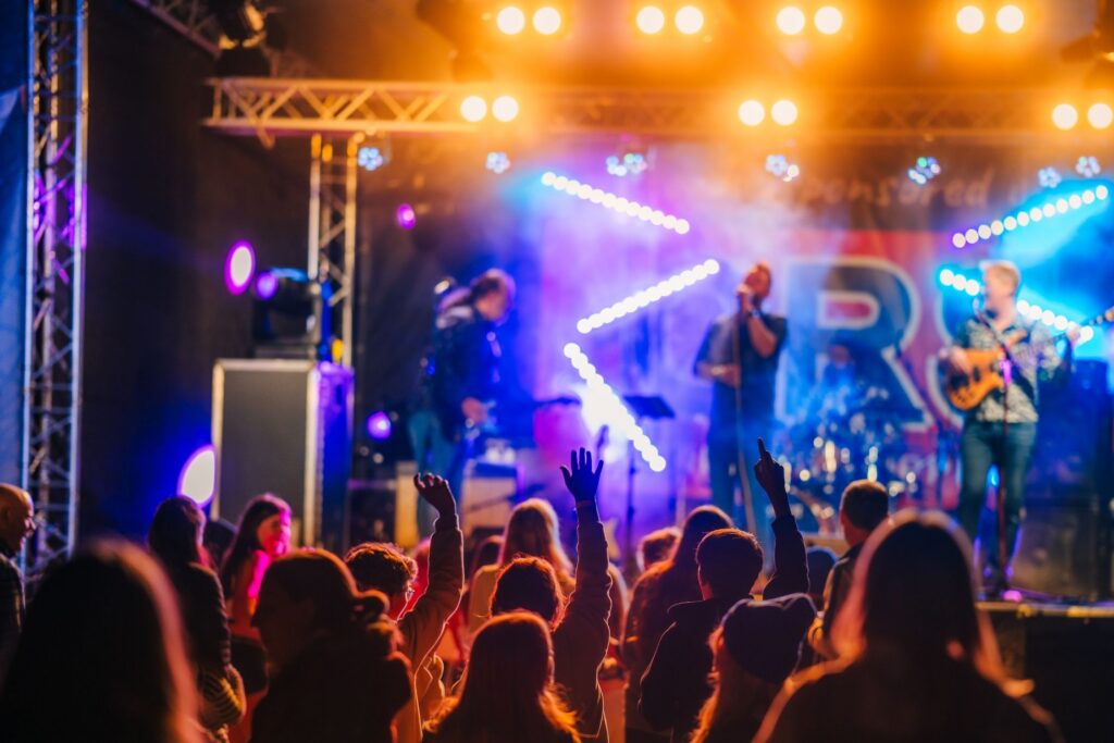 A crowd of p[eople, some with their arms in the air, watching three members of a band on stage