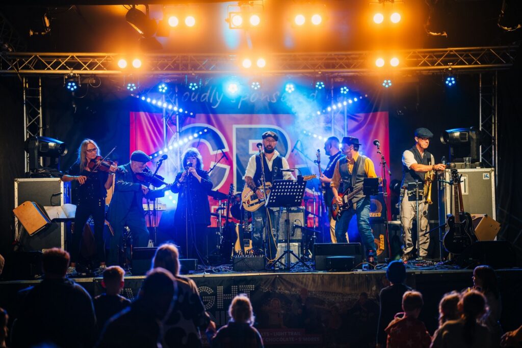 A seven person folk band on stage in front of an audience at The Mendip Festival
