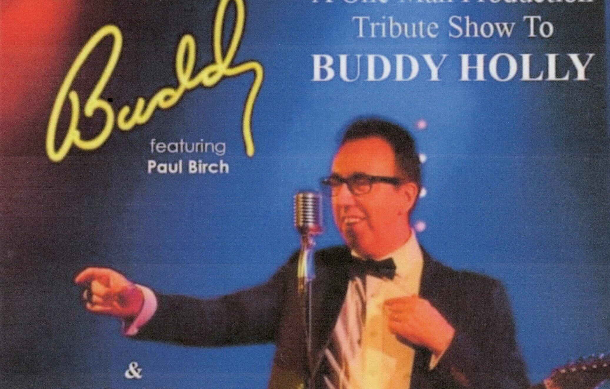 A singer in a dark suit and wearing glasses points as he sings into a microphone