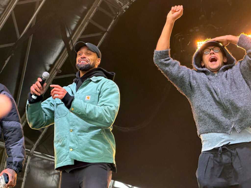 Two band members perform on stage with the one on the right rasiing his arm in celebration