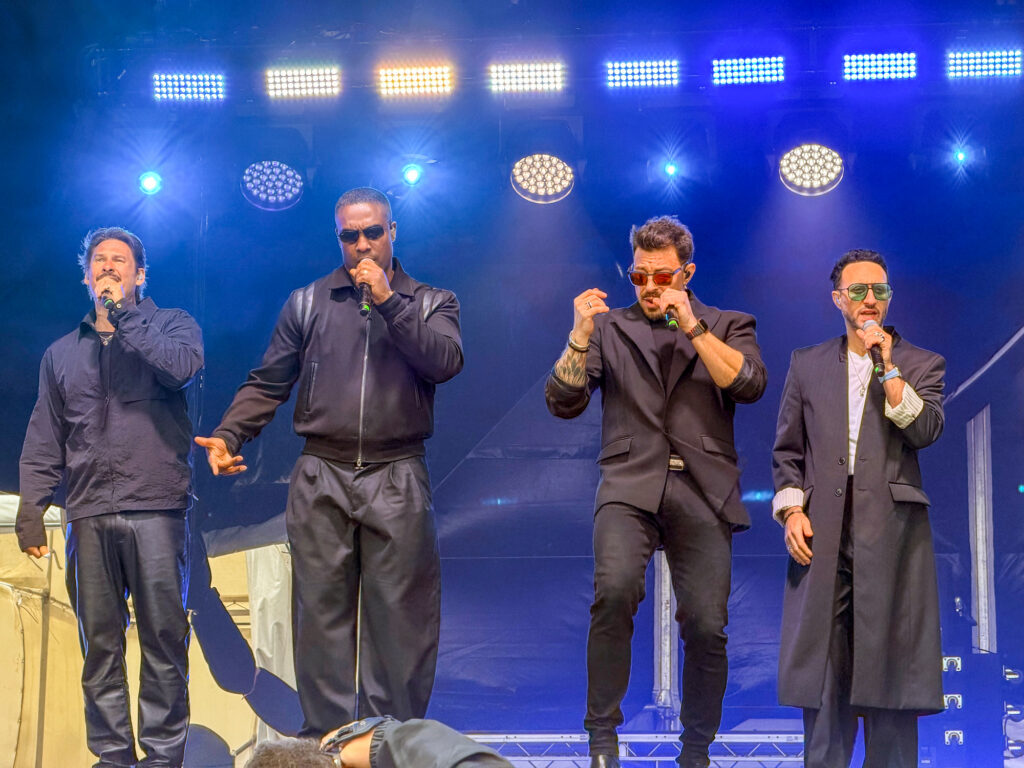 Four member of a boy band all wearing dark clothing perform on stage