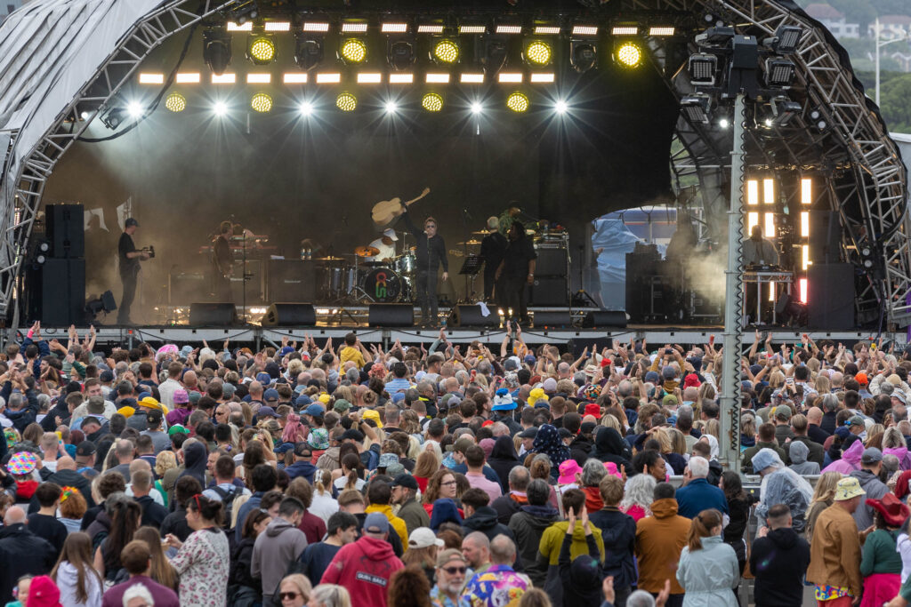 A huge crowd watching a band on a large outdoor festival stage