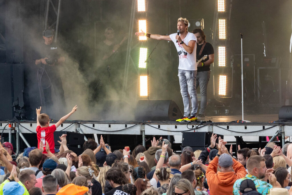 The lead singer of a band addressess the large crowd in front of him including a young boy who is stitting on somebody's shoulders