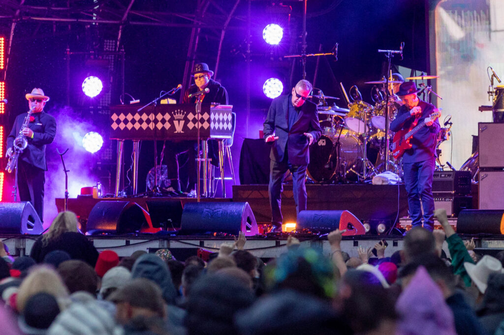 Wide angle view of a band performing on stage with the crowd in the foreground