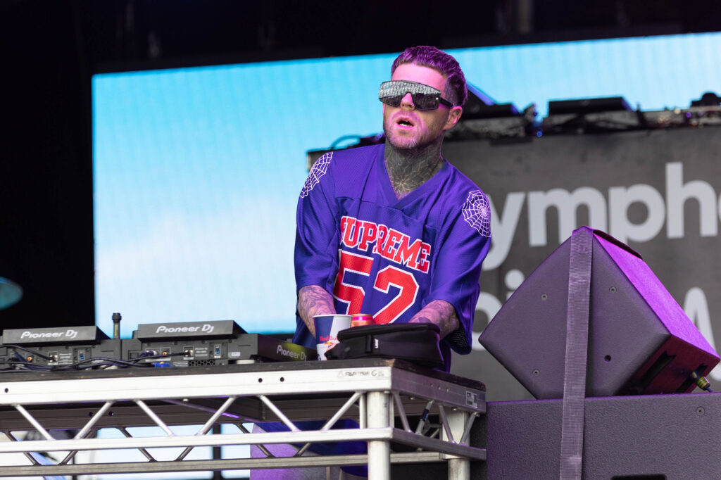 A man in a blue and red American football shirt works the decks at a concert