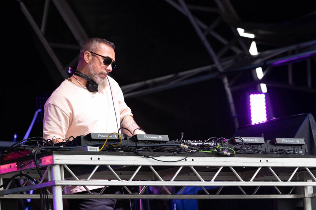 A man in white t-shirt and dark sunglasses on the DJ decks