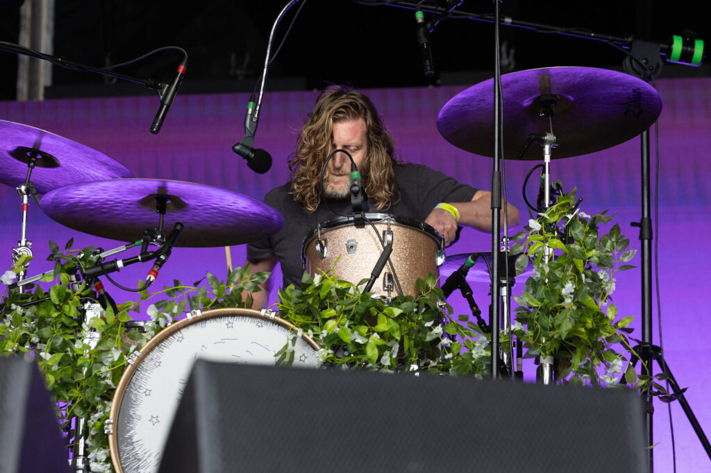 A drummer on stage with lots of greenery around his drum kit