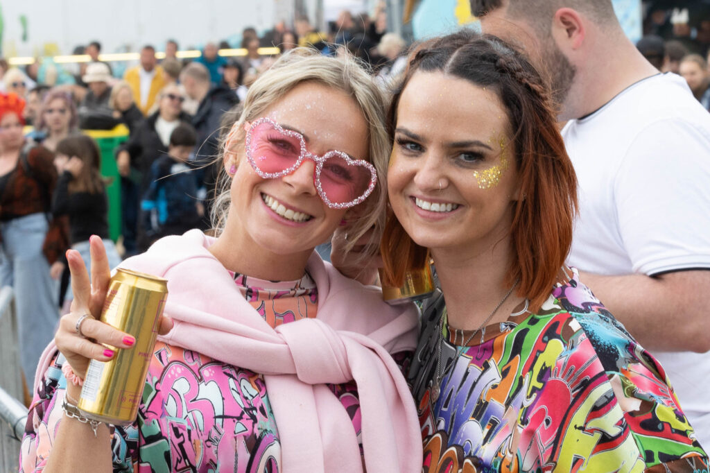Two female festival goers one with glitter sunglasses and the other with glitter on her face