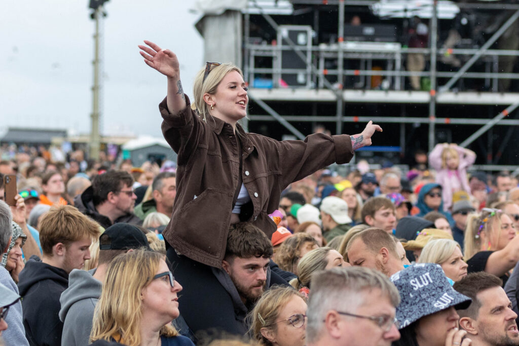 A festival goer with her arms outstretched sits on a man's shoulders to get a better view