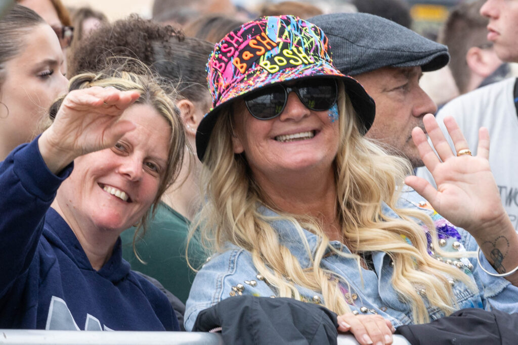 A female festival goer in a multi coloured hat waves