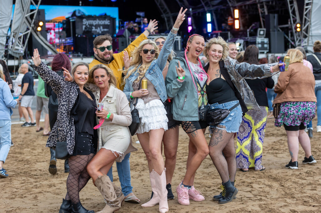 A large group of festival goers on the sand in front of the stage