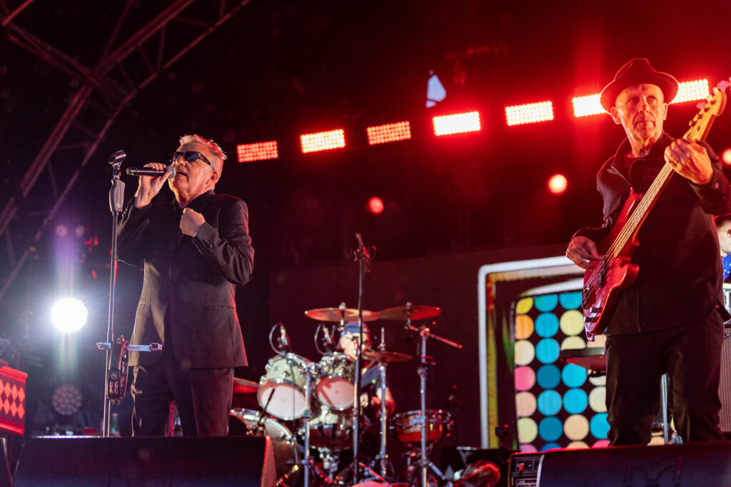 A singer and guitarist both in dark suits on stage