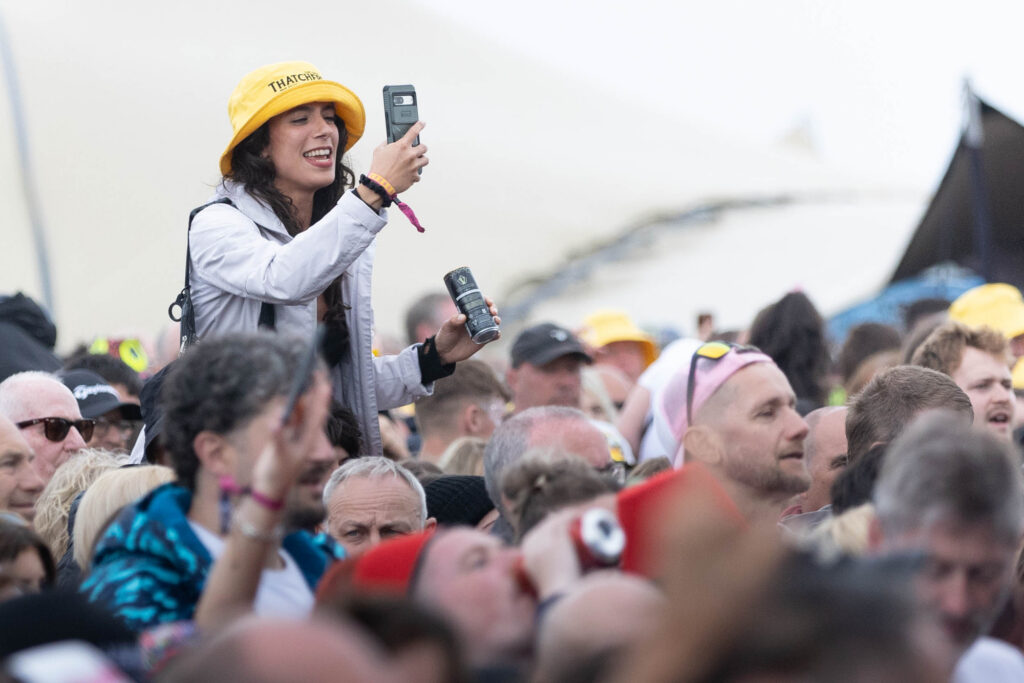 A festival goer takes mobile phone pics above the crowd while sitting on someone's shoulders