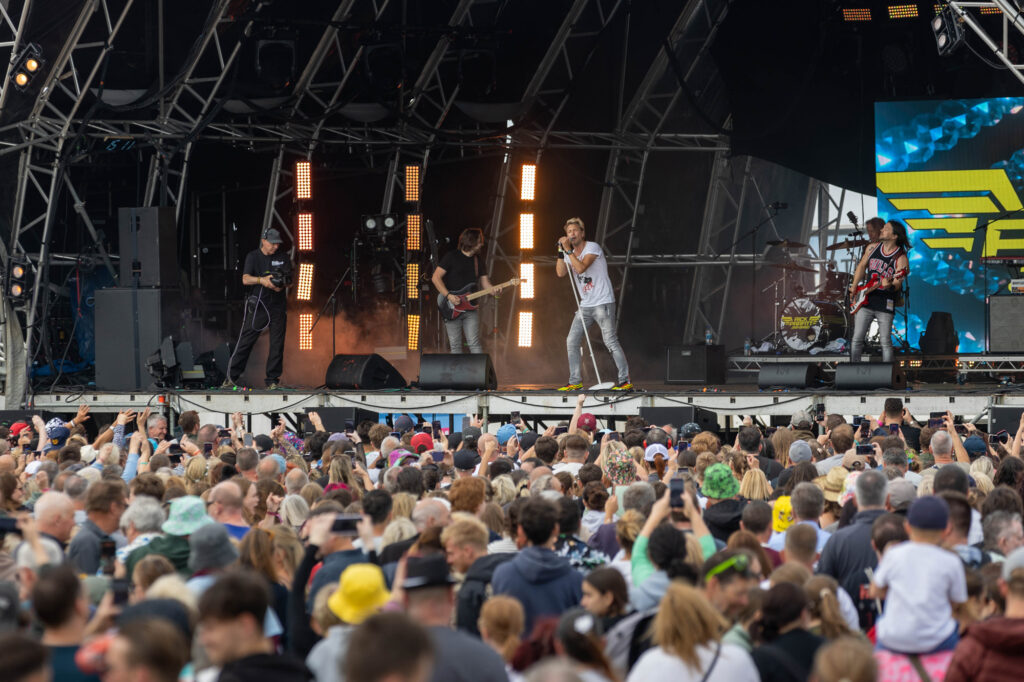A large crowd watching a band in the distance on a large stage