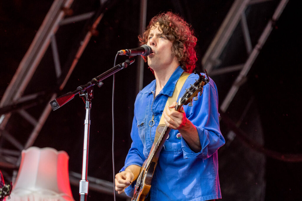 A guitarist in a blue shirt sings into his microphone