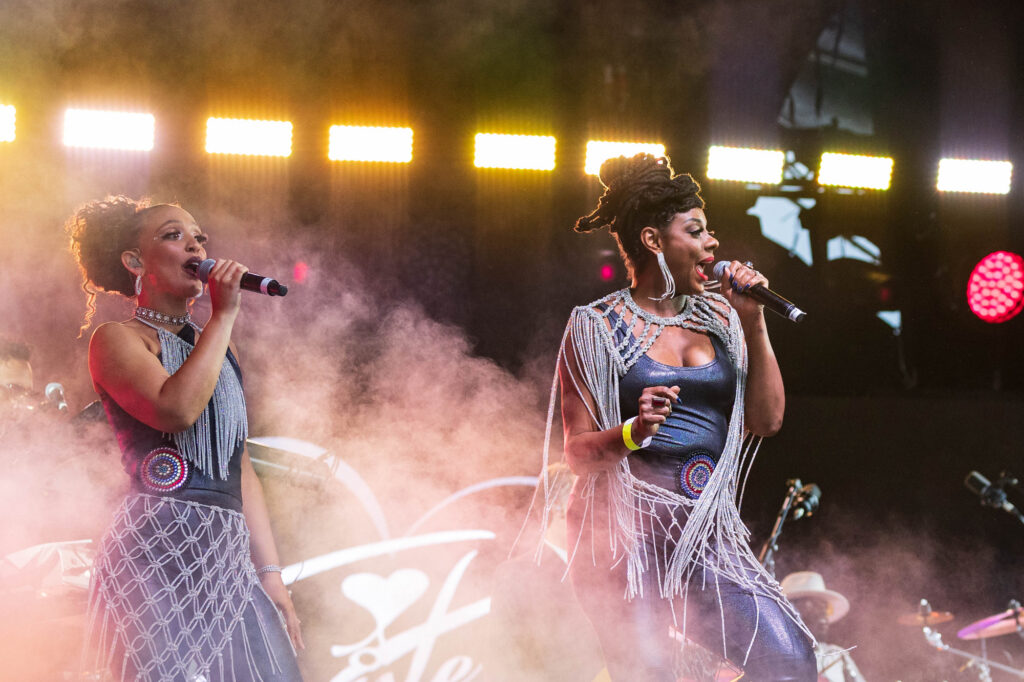 Two members of Sister Sledge perform on stage as stage smoke billows around them