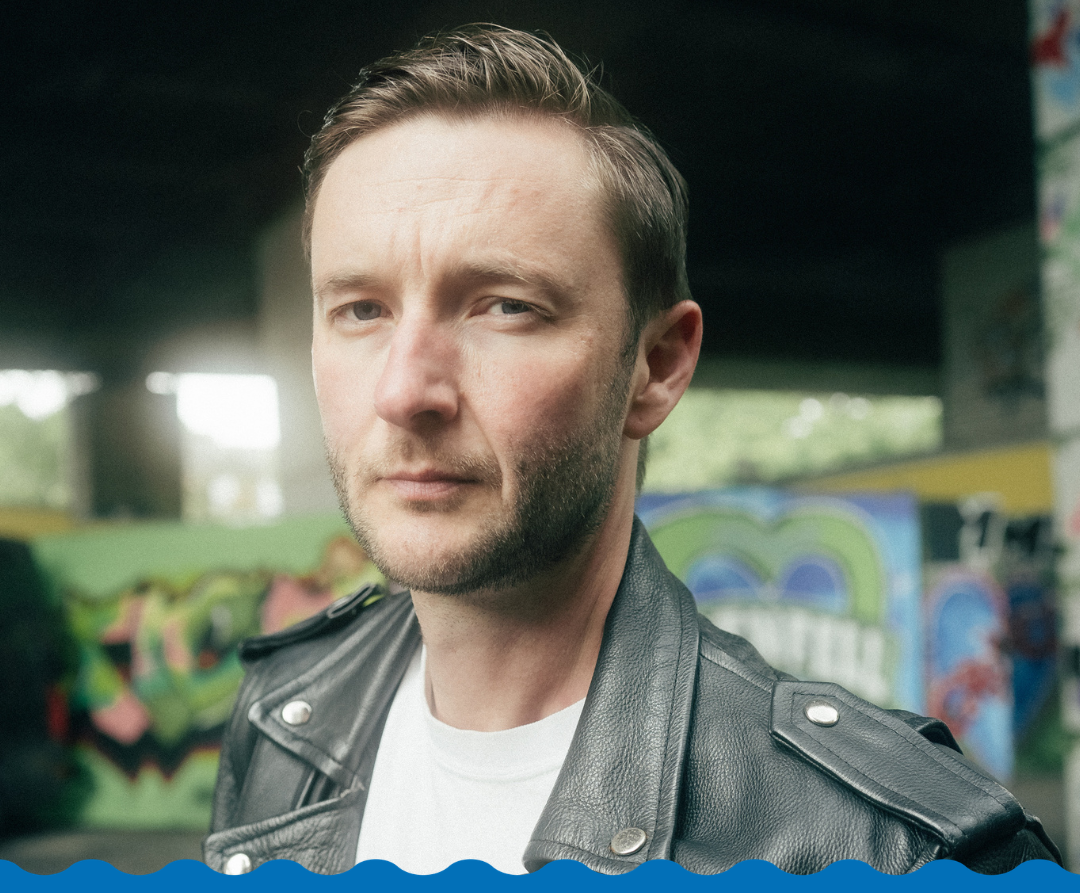 A man in a leather jacket looks towards camera