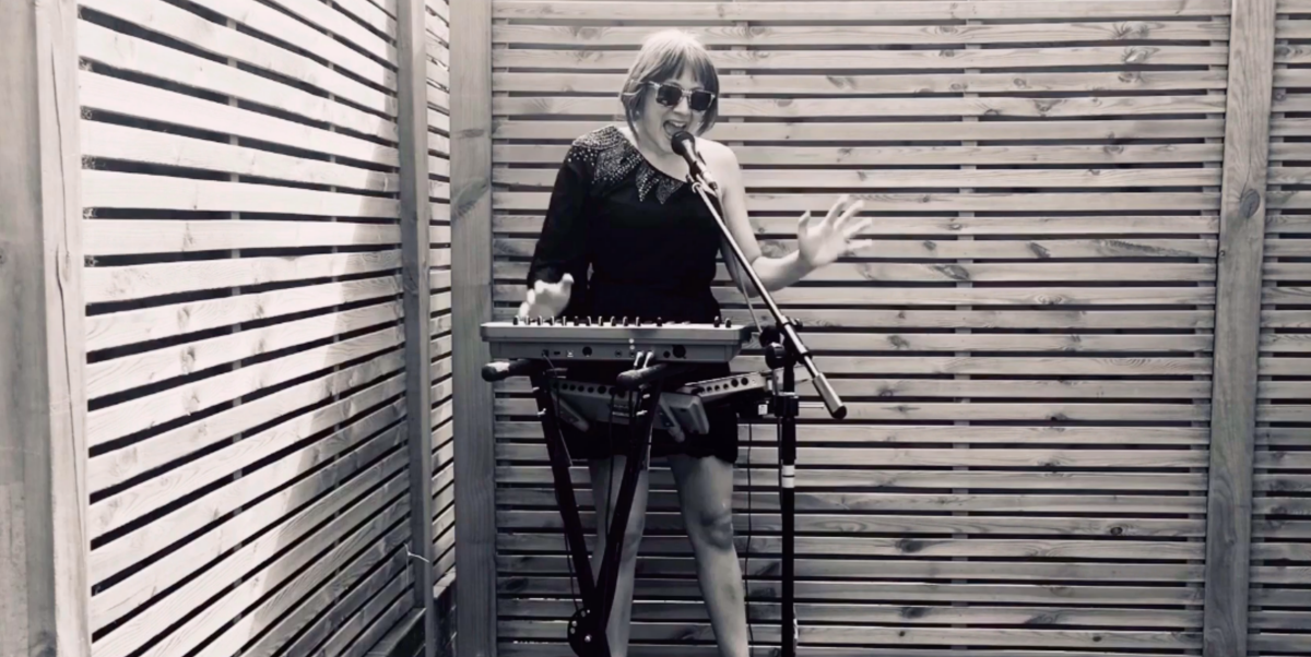 A woman stands behind an electronic keyboard and microphone