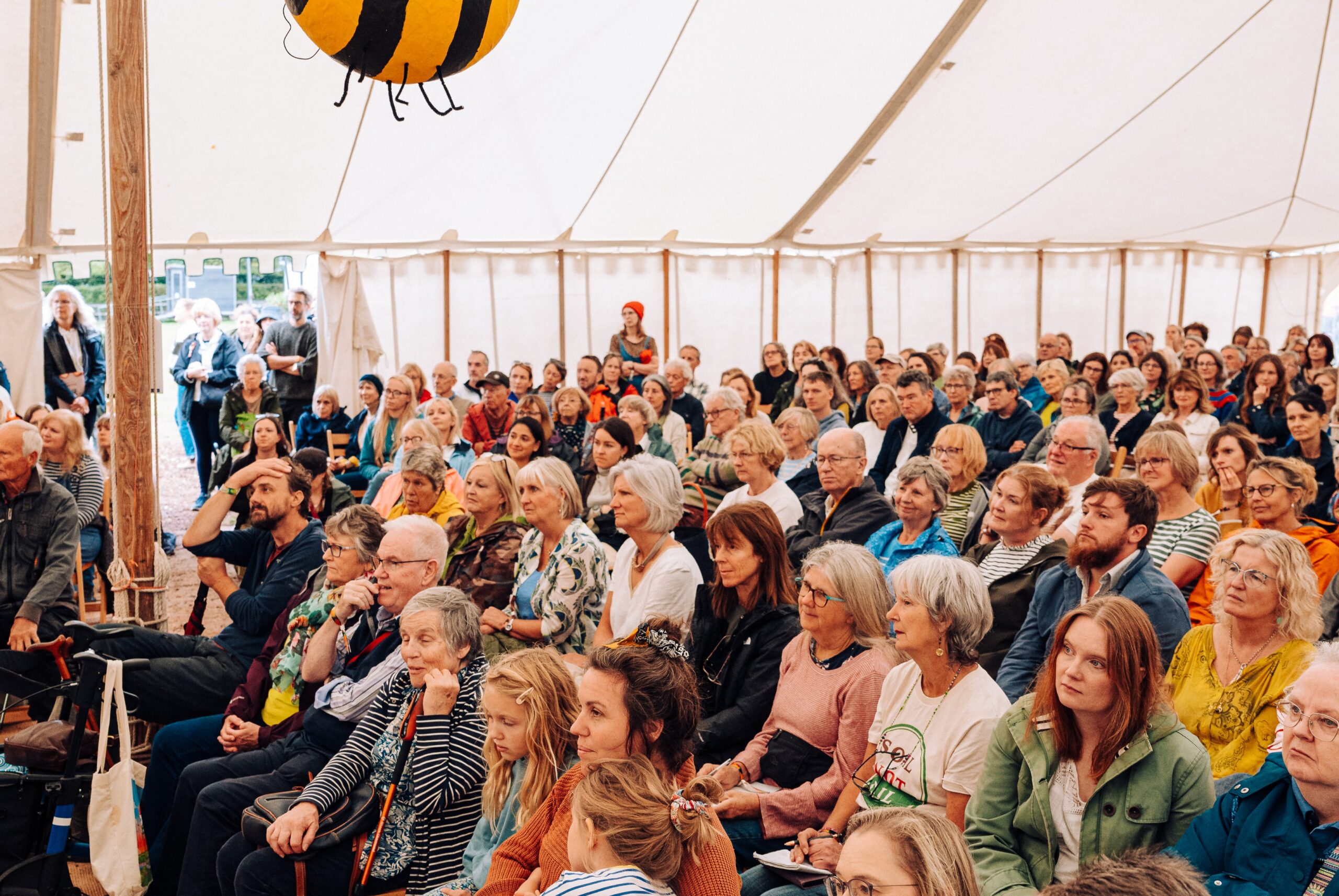 A group of people sit in rows in a canvas tent