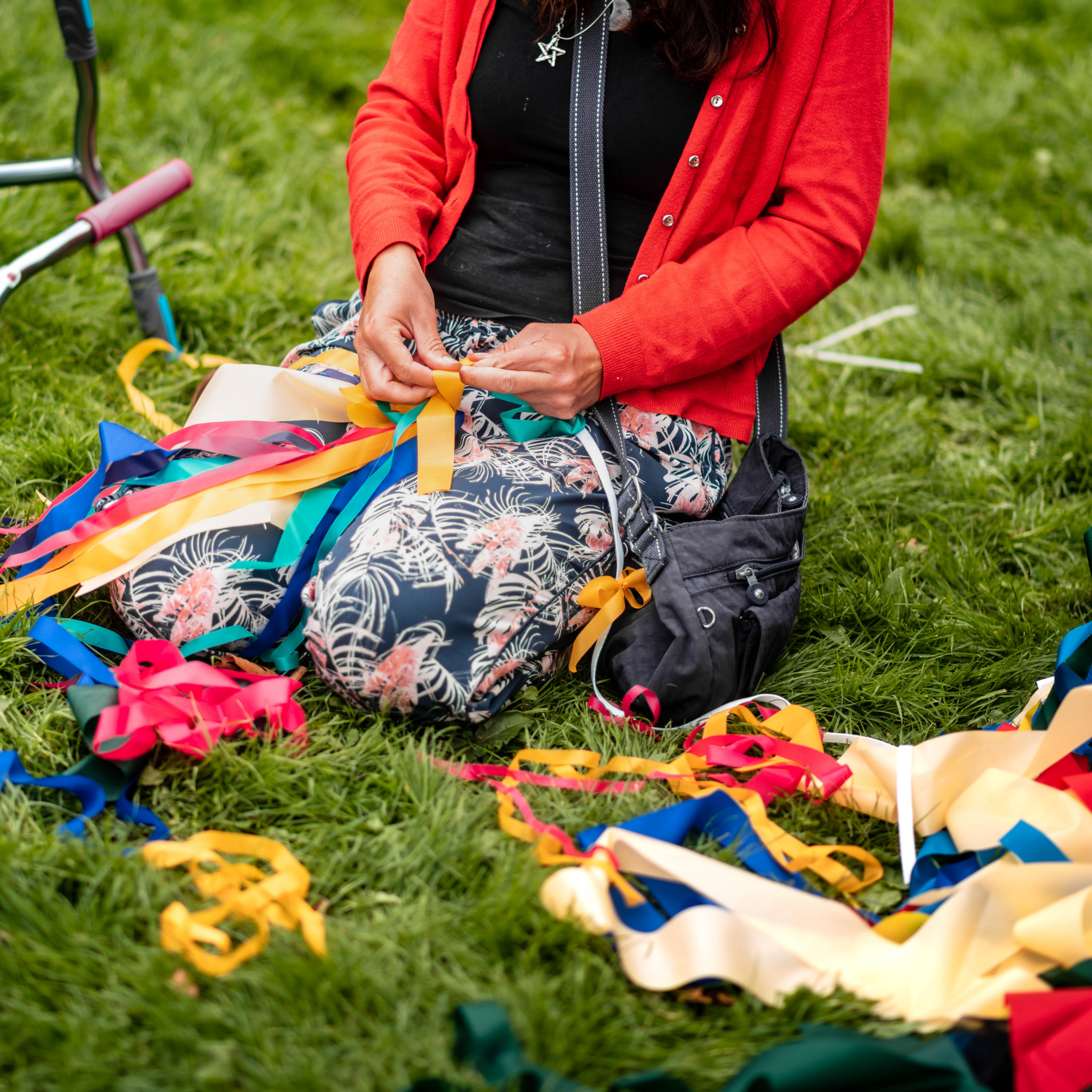 A person kneels on grass with lots of ribbons and material around them