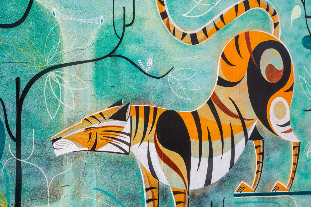 Street art of a gold, brown, white and yellow cat-like creature on a green wall