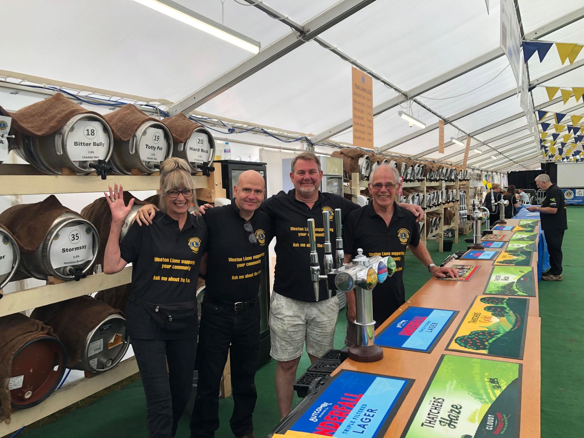 A group of people stand in a line in front of lots of beer barrels stacked high