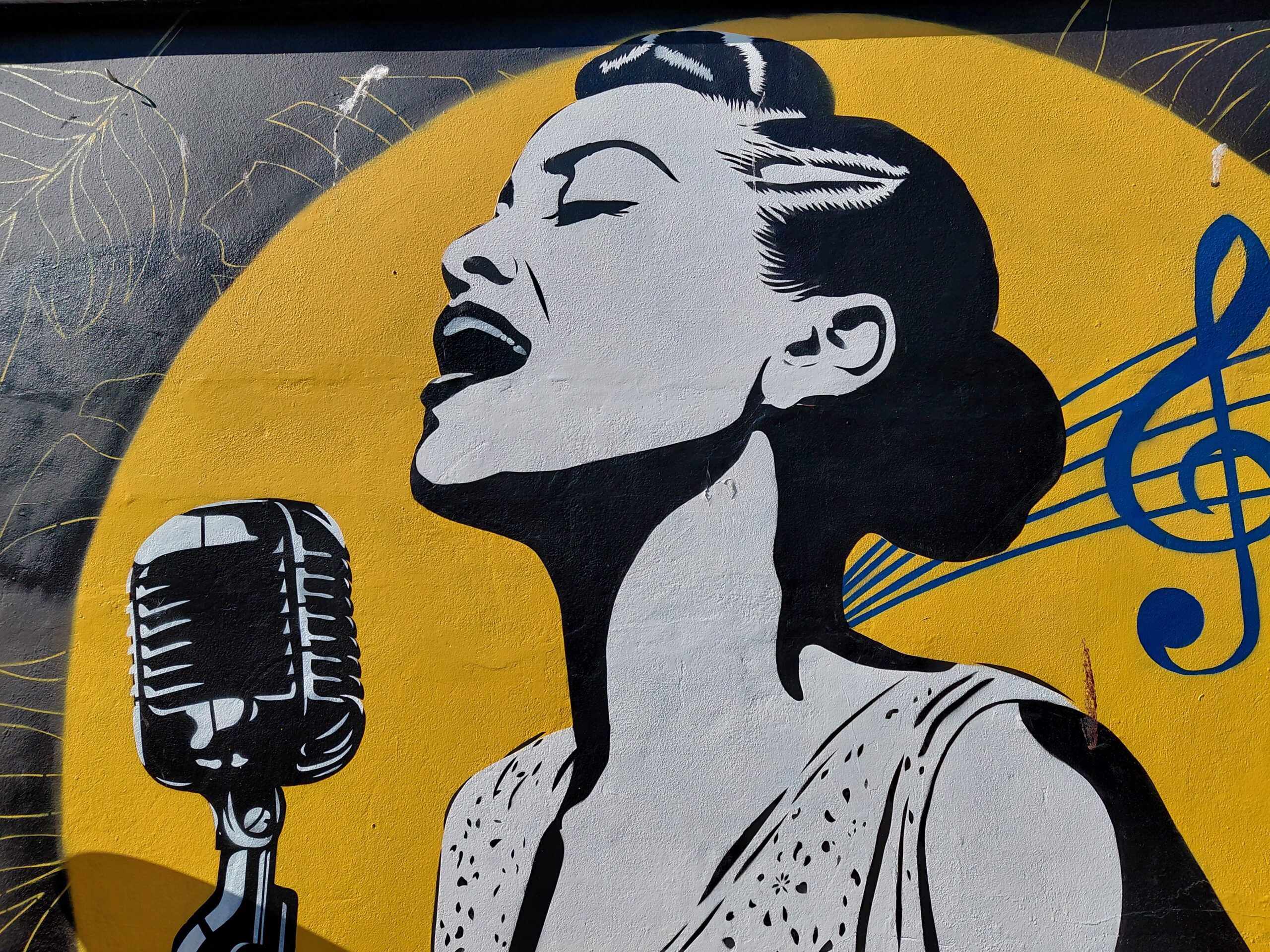 Mural of a black and white 50s style female singer performing into a vintage microphone while set against a yellow background