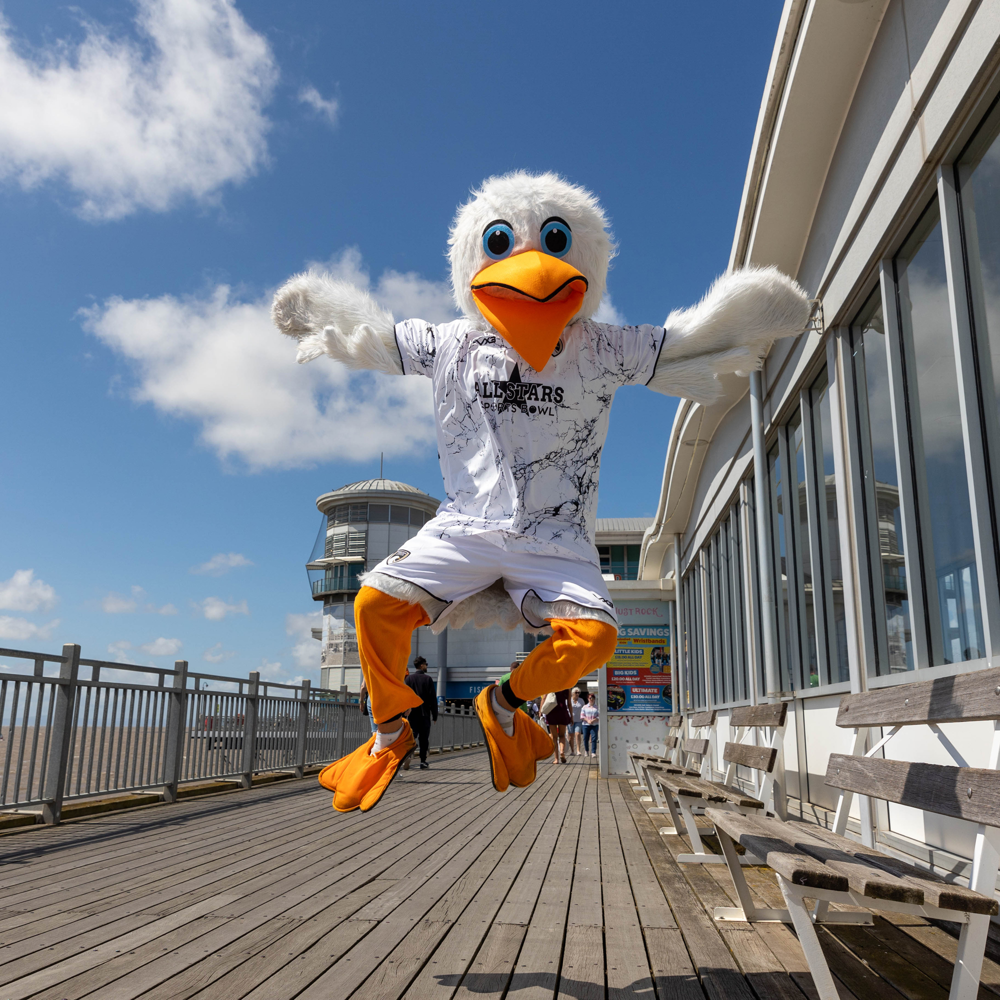 A large seagull mascot jumps into the air on the boardwalk of a pier