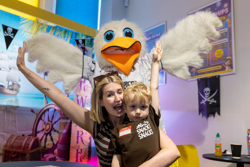A mum and young boy flap their arms like wings as a giant seagull mascot stands behind them