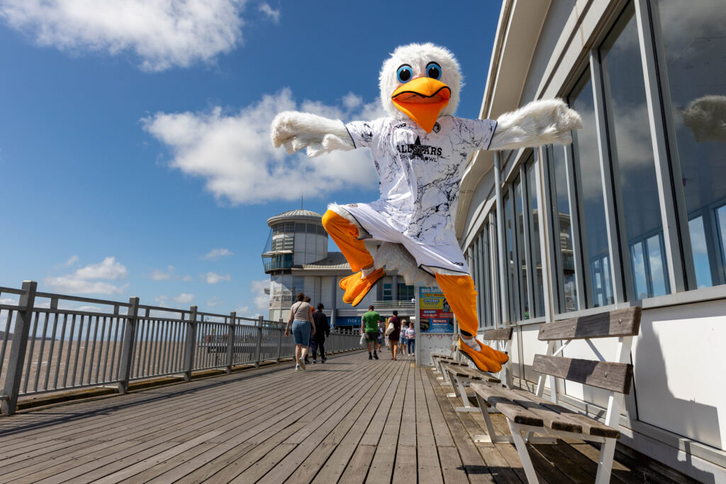 A giant seagull mascot jumping into the air on a pier