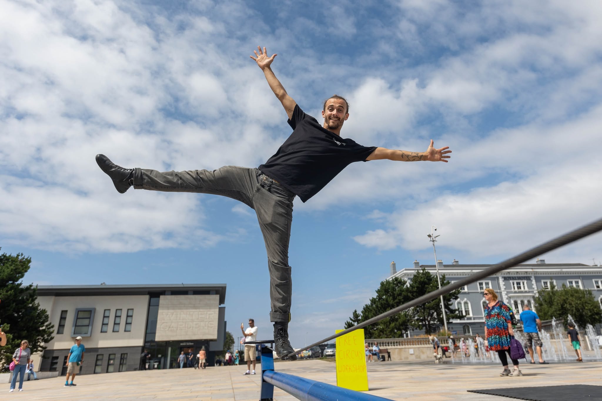 A man in a black t -shirt and dark jeans standing on one leg on a tightrope