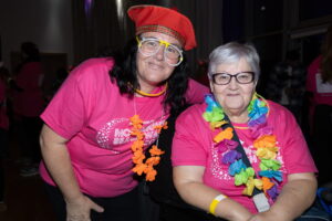 Two ladies stand together wearing pink shirts and flower garlands