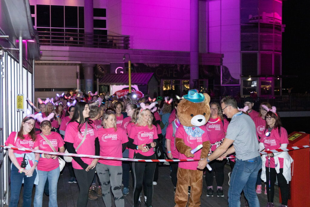 A group of people wearing pink shirts stand behind a starting line. There's also someone dressed as a bear