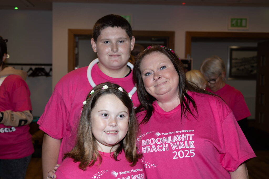 A lady, girl and boy stand together wearing pink shirts