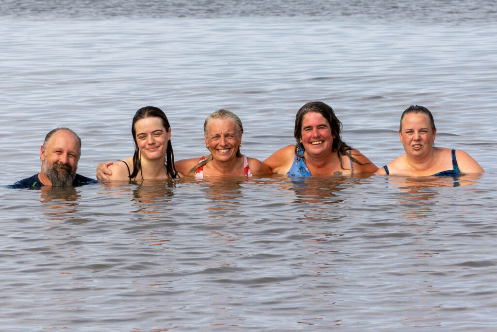 One man and four women all shoulder to shoulder in the sea with just their faces and shoulders above water