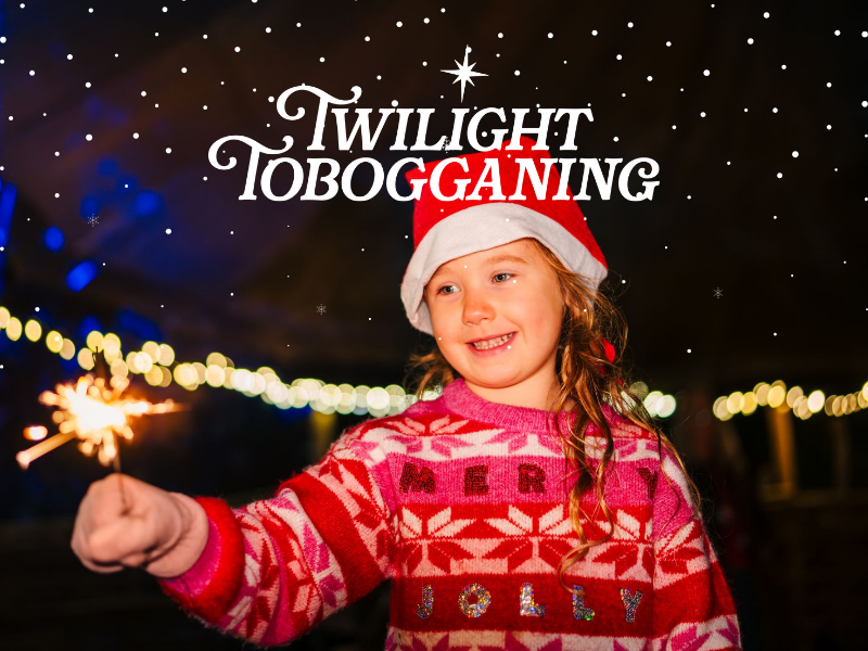 A girl in christmas hat and jumper stands holding a sprinkler
