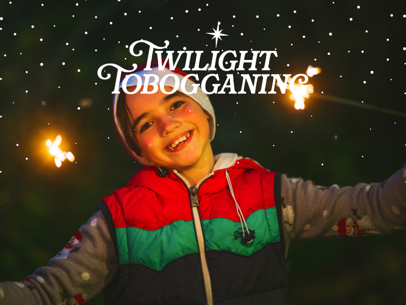 A boy in winter clothing stands with arms open as sparklers shine behind him