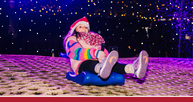 A girl rides a toboggan down a slope. They're dressed in winter clothing