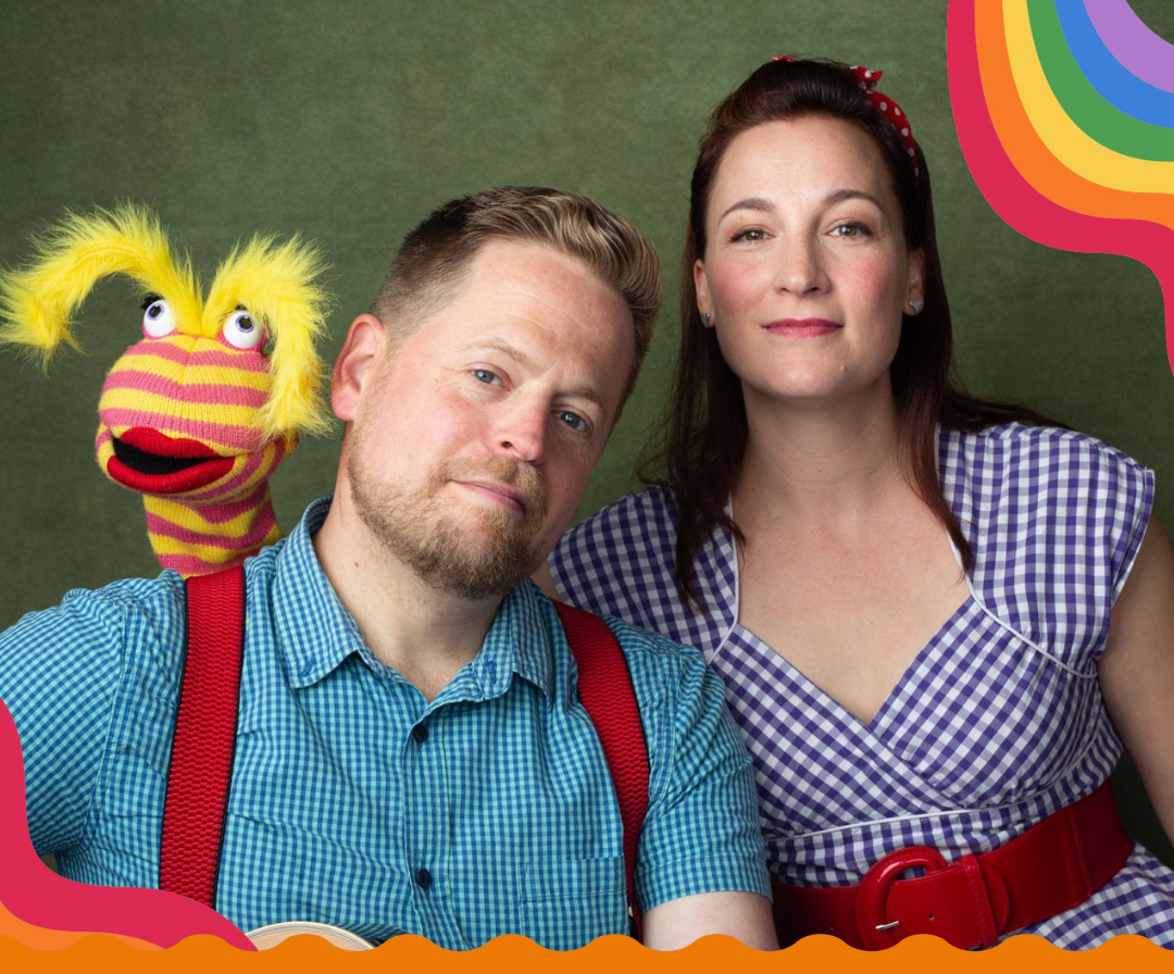 A man and woman stand shoulder to shoulder. Behind them a yellow and pink stripey sock puppet stands