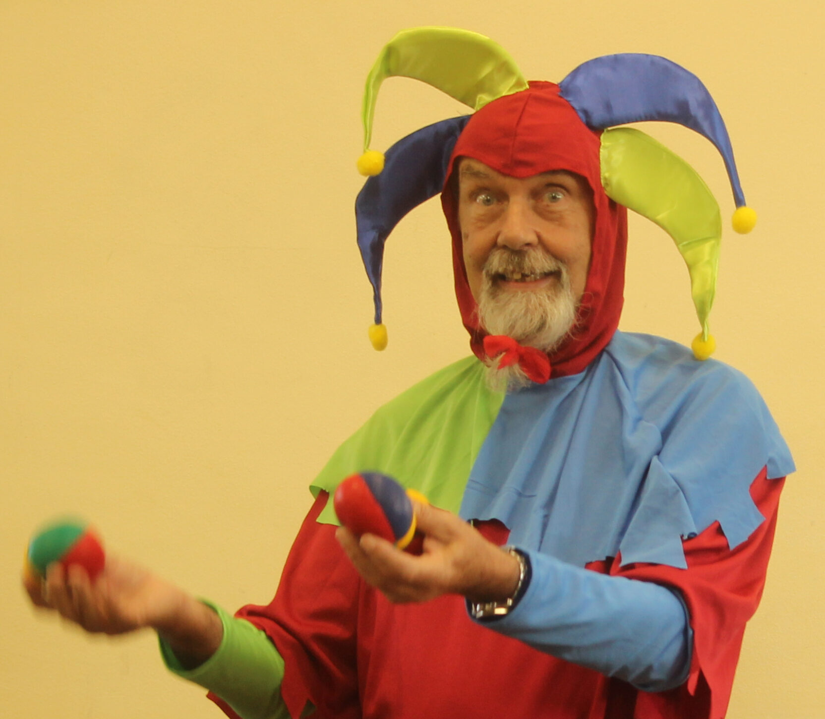A man dressed as a classic medieval jester, in red, yellow, blue and green, holding juggling balls