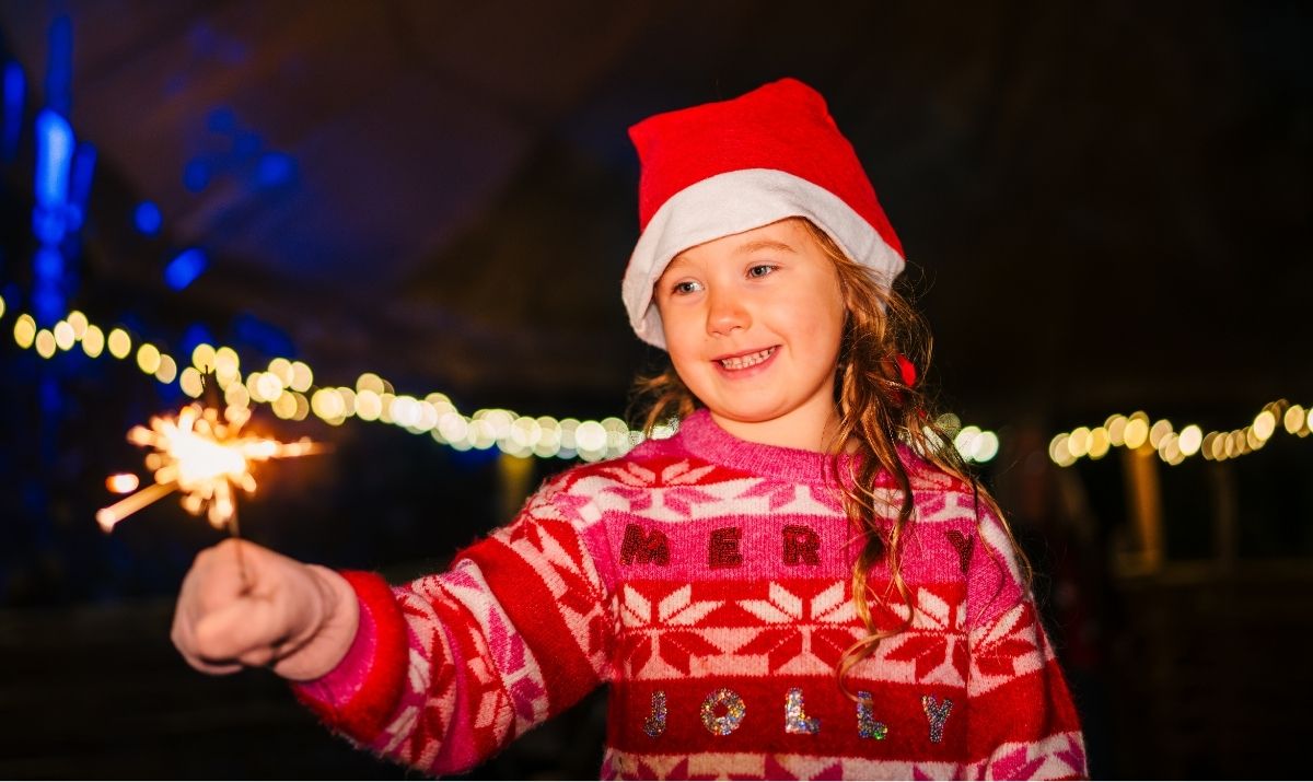 A young girl in a red santa hat and jumper holding a sparkler
