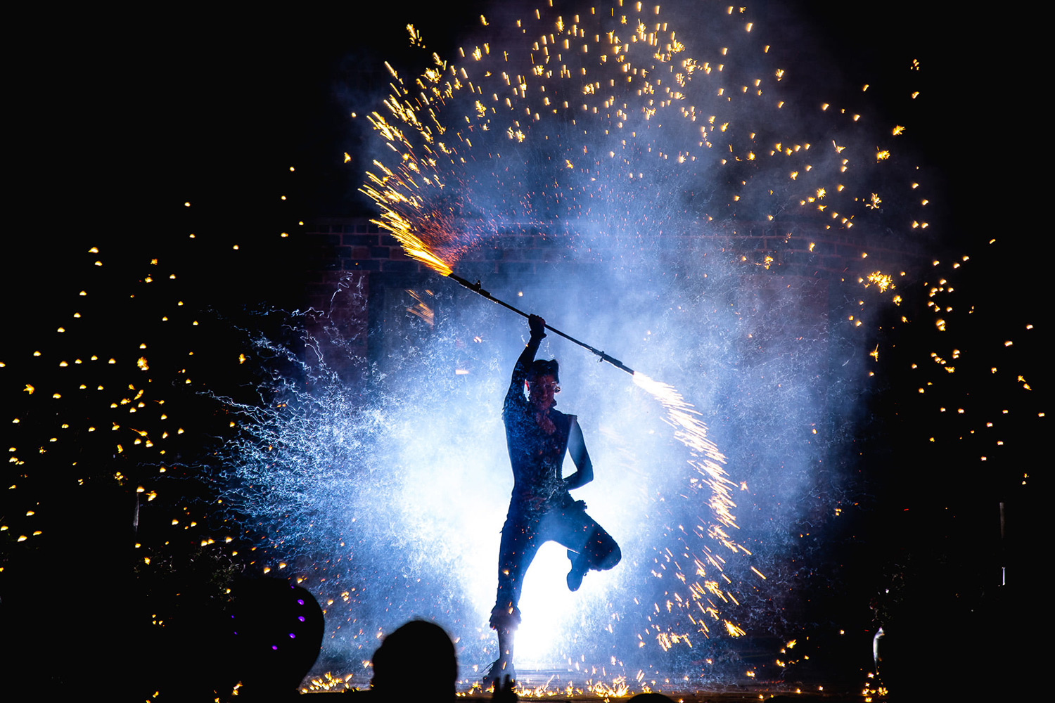 Silhouette of a man twirling a flaming baton with sparks coming off it, set against the night sky